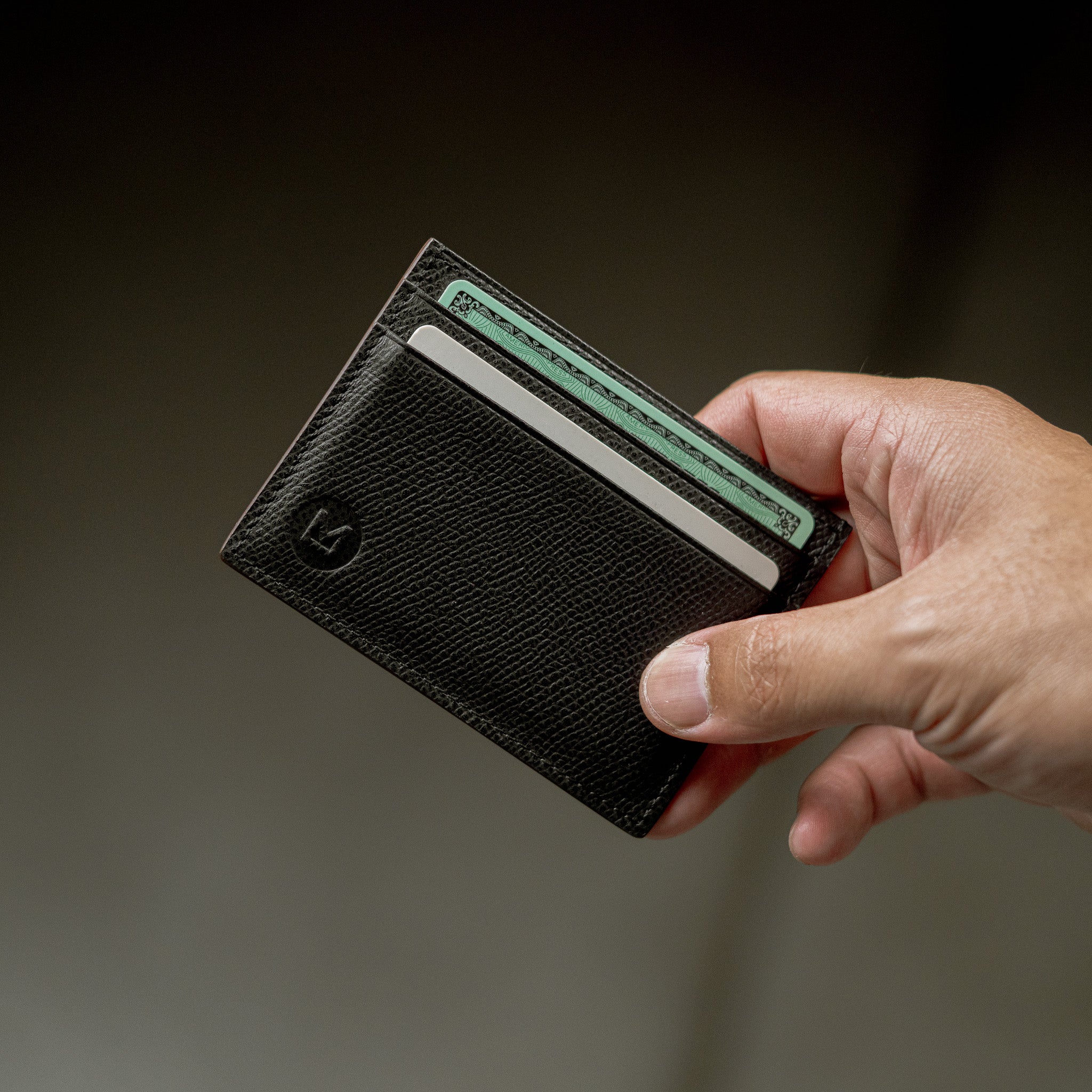 Hand holding a black leather wallet with a card inside on a dark background